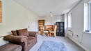 Living room with sofas, dining table, shelving unit and windows.