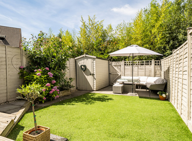 Garden with a lawn, planting beds, shed and outdoor seating area.