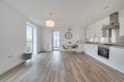 Bright open-plan living and kitchen space with wood-effect flooring, white walls, and large windows