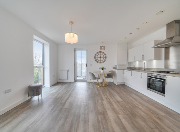 Bright open-plan living and kitchen space with wood-effect flooring, white walls, and large windows