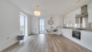 Bright open-plan living and kitchen space with wood-effect flooring, white walls, and large windows