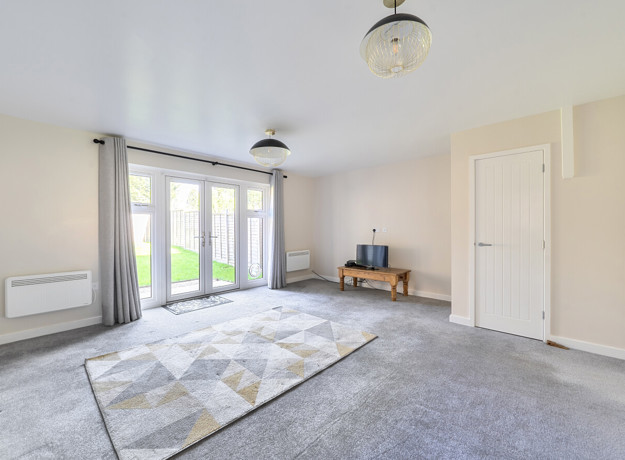Bright living room with grey carpet, patterned rug and French doors to garden