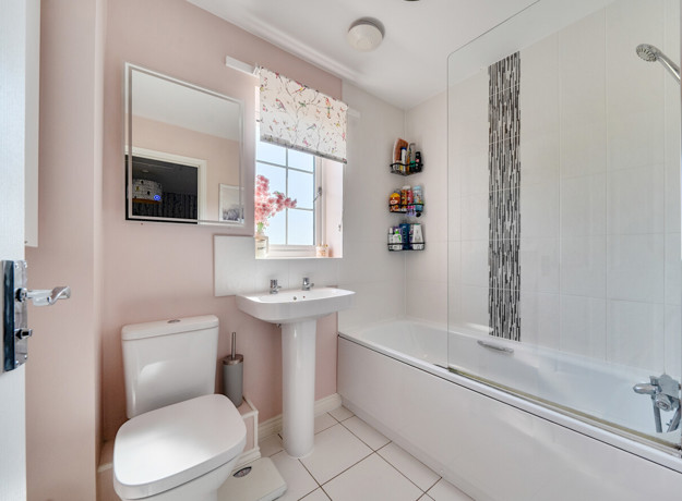 Bathroom with toilet, pedestal sink and bathtub with shower screen.