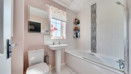 Bathroom with toilet, pedestal sink and bathtub with shower screen.