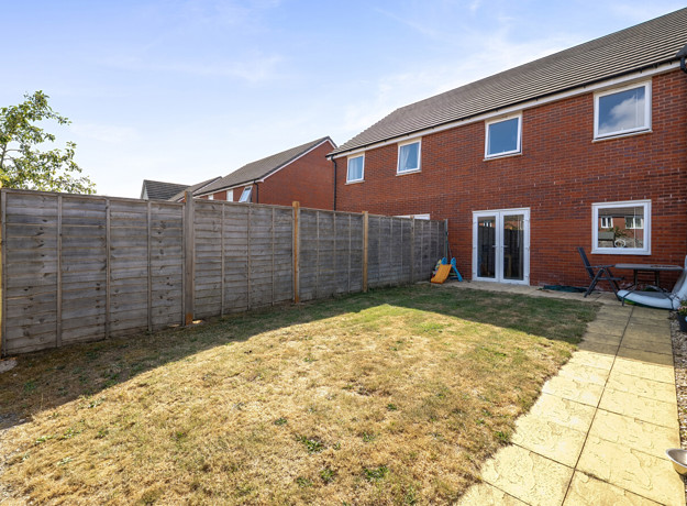 Enclosed rear garden with lawn, paved path, and wooden fencing.