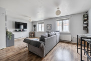 Open living room with sofas, TV unit, window and wooden-effect flooring.