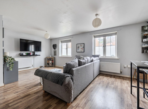 Open living room with sofas, TV unit, window and wooden-effect flooring.
