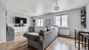 Open living room with sofas, TV unit, window and wooden-effect flooring.