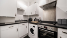Kitchen with integrated appliances, white units, and tiled backsplash.