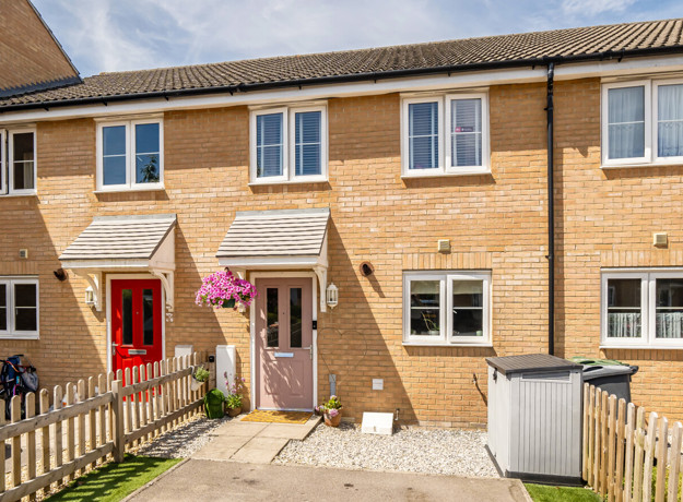 A brick terraced house with front garden, pink front door and paved access path.