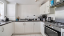 Modern white kitchen with cabinets, gas hob, and black countertops.
