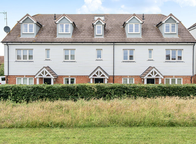 Row of terraced houses with white walls and grass area in foreground.