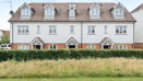 Row of terraced houses with white walls and grass area in foreground.