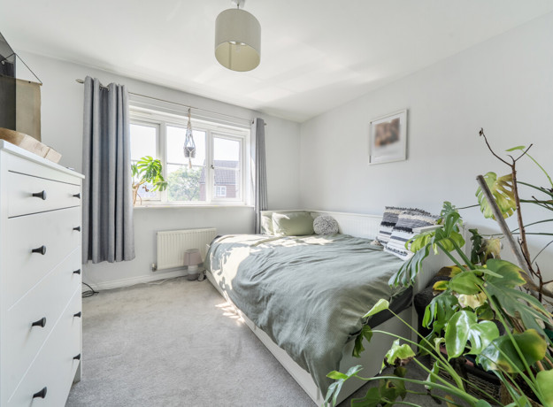 Bedroom with bed, white furniture, and plants by the window.