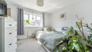 Bedroom with bed, white furniture, and plants by the window.