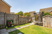 Garden with a lawn, paved path, fencing, trampoline and wooden shed.