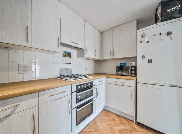 Bright fitted kitchen with light wood cabinets, wood-effect worktops, integrated oven, and freestanding fridge freezer.