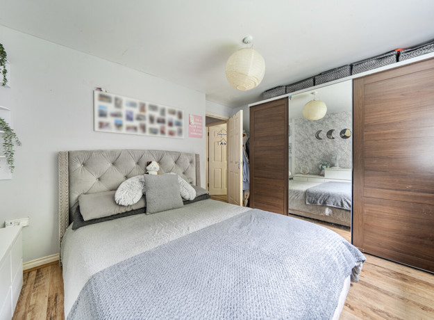 Bedroom with bed, wardrobe, wall decor and wooden-effect flooring.
