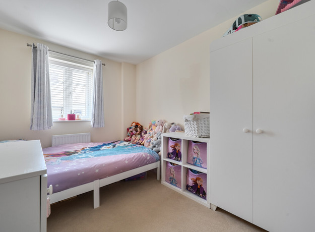 Child's bedroom with single bed, wardrobe, shelving, and window with curtains.