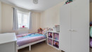 Child's bedroom with single bed, wardrobe, shelving, and window with curtains.