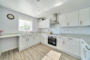Modern fitted kitchen with white units, integrated oven and wood effect flooring