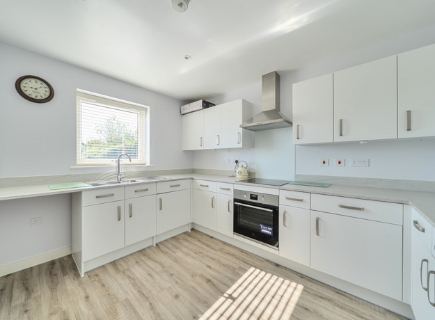 Modern fitted kitchen with white units, integrated oven and wood effect flooring