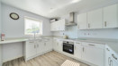 Modern fitted kitchen with white units, integrated oven and wood effect flooring
