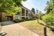 Apartment building with balconies, surrounded by trees and a paved path.