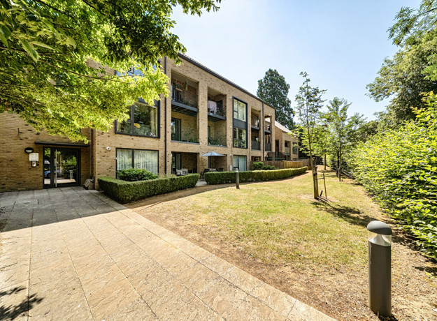 Apartment building with balconies, surrounded by trees and a paved path.