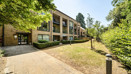Apartment building with balconies, surrounded by trees and a paved path.