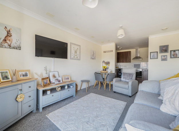 Open-plan living area with sofas, a TV and dining space, leading into kitchen.