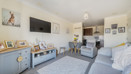 Open-plan living area with sofas, a TV and dining space, leading into kitchen.