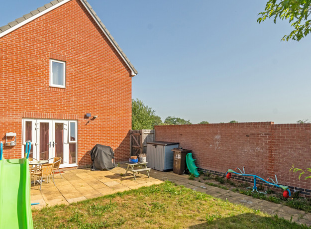 Rear garden with lawn, patio area and brick house exterior.