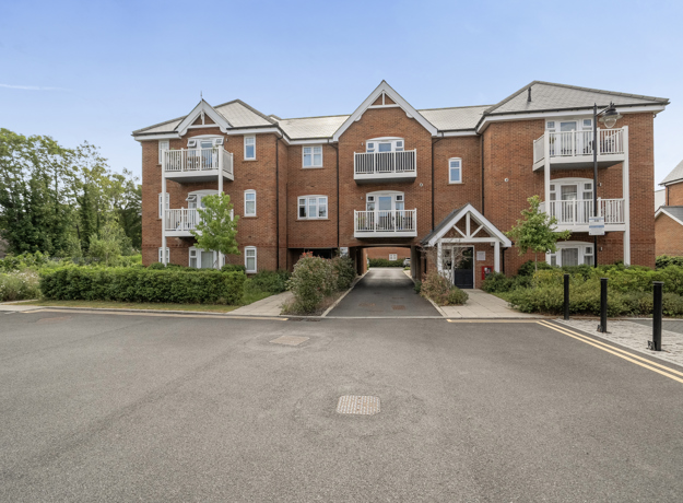 Modern brick apartment building with pitched roofs, entrance doors, and parking area.