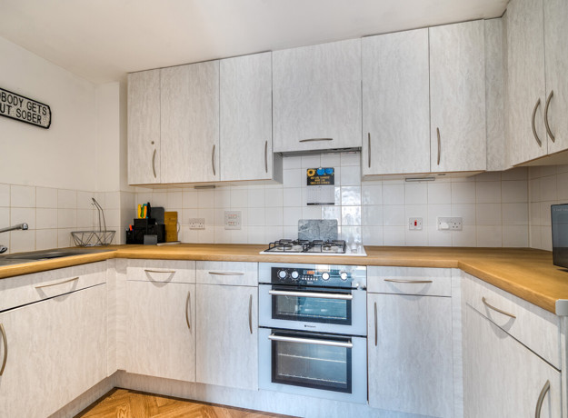 L-shaped kitchen with light cabinetry, tiled splashback, electric cooker, and wood-effect countertops.