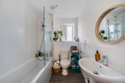 Bathroom with bathtub, sink, round mirror, and white tiled walls.
