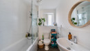 Bathroom with bathtub, sink, round mirror, and white tiled walls.