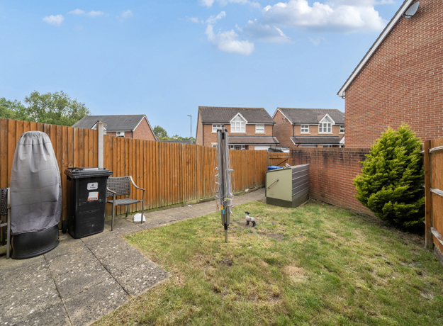 Garden with paving slabs, lawn, wooden fence, and bins near the patio.