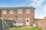 Rear view of brick house with fenced garden and small patio area.