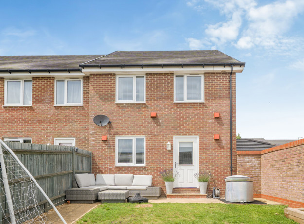 Rear view of brick house with fenced garden and small patio area.