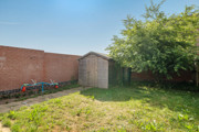 Enclosed garden with grass lawn, wooden shed and surrounding fences.
