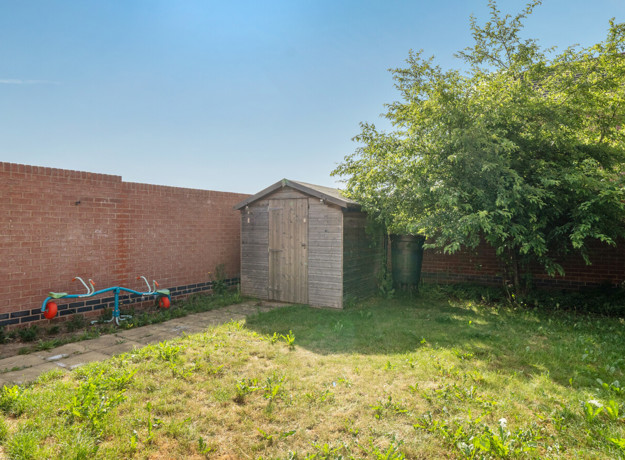 Enclosed garden with grass lawn, wooden shed and surrounding fences.