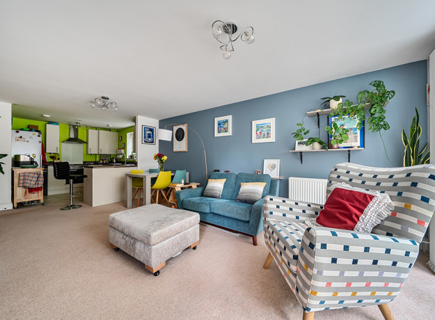 Open-plan living area with armchairs, sofa and breakfast bar leading into kitchen.