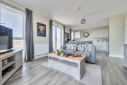 Open-plan living area with sofas, television, and kitchen in the background.