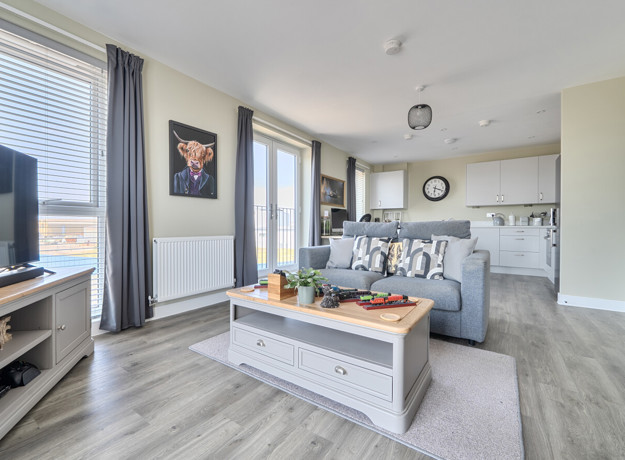 Open-plan living area with sofas, television, and kitchen in the background.