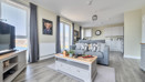 Open-plan living area with sofas, television, and kitchen in the background.