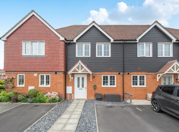 Row of brick and render terraced houses with parked car on a driveway.