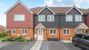 Row of brick and render terraced houses with parked car on a driveway.