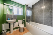 Bathroom with green walls, pedestal sink, toilet, and bathtub with shower screen.