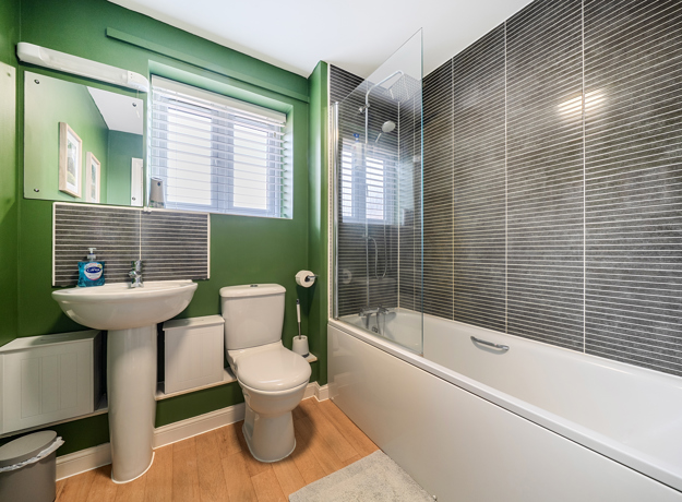 Bathroom with green walls, pedestal sink, toilet, and bathtub with shower screen.